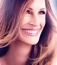 a close up of a person with long hair and wearing a white shirt smiling at the camera