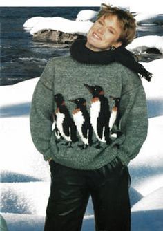 a man standing in the snow wearing a sweater with penguins on it