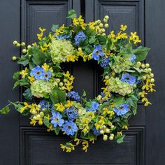 a wreath with blue, yellow and green flowers is hanging on a black front door