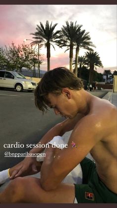 a shirtless man sitting on the side of a road with palm trees in the background