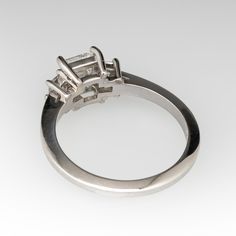 This bright ring is centered with one (1) rectangular step cut diamond weighing 1.02 carats set in four-prongs. Accenting either side of the center stone is one (1) square step cut diamond that is prong set. The ring measures 7.3mm at the top, rises 5.5mm above the finger, tapering to 2.0mm wide and 1.8mm thick at the base of the shank. This platinum ring currently fits a size 6.5. Emerald Cut Diamond Engagement, Emerald Cut Diamond Engagement Ring, Emerald Cut Diamond Ring, Platinum Diamond Engagement Rings, Engagement Rings Bridal Sets, Platinum Engagement Rings, Platinum Ring, Emerald Cut Diamonds, Emerald Cut