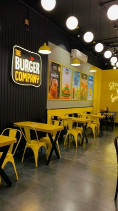 the inside of a restaurant with yellow tables and black chairs, neon signs on the wall