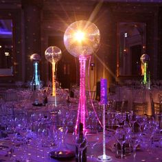 a room filled with lots of tables covered in purple and white table cloths next to tall glass vases