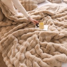 a woman is holding a coffee cup while laying on a bed covered in fluffy blankets