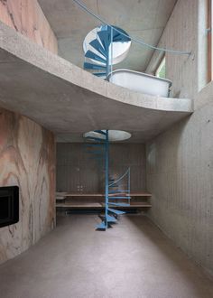 a spiral staircase in the middle of a room with concrete walls and floor to ceiling windows