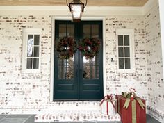 two christmas wreaths on the front door of a house with presents in front of it