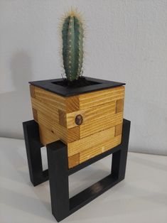 a wooden planter with a cactus in it sitting on a black stand next to a white wall