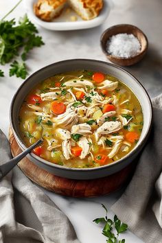 a bowl of chicken noodle soup with bread and parsley