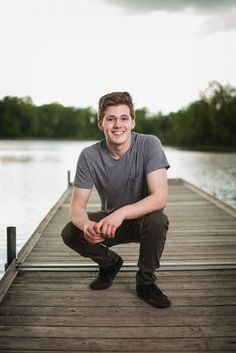 a young man is sitting on a dock by the water