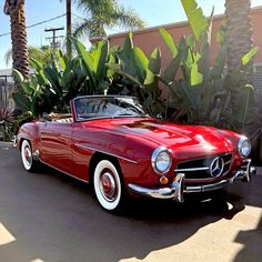 an old red convertible car parked in front of a house with palm trees behind it