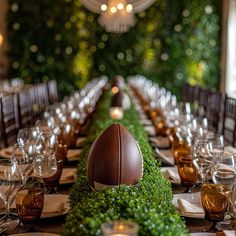 the table is set with an arrangement of greenery, candles, and football shaped centerpieces