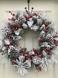 a wreath with pine cones and red berries hanging from the front door, decorated for christmas