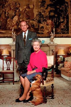 a man and woman sitting next to a dog in front of a painting on the wall