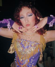 a woman with red hair wearing a purple and gold costume is posing for the camera