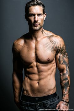 a shirtless man with tattoos on his chest posing for a photo in front of a gray background