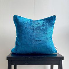 a blue velvet pillow sitting on top of a wooden chair next to a white wall