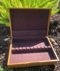 an open box with several pieces of wood in it on the ground next to some plants