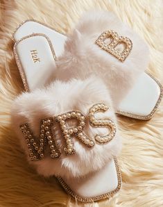 a pair of white slippers with the word mrs written on them, sitting on a fur rug