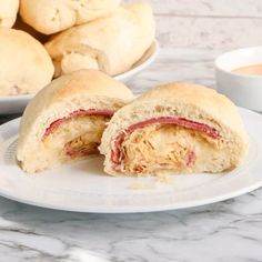 a sandwich cut in half on a plate next to some dipping sauce and bread rolls