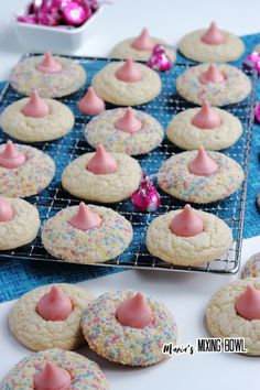 cookies with pink frosting and sprinkles are on a cooling rack next to some candy