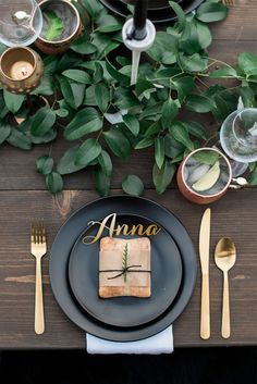 a black plate topped with a piece of cake next to utensils and greenery