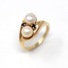 Classic vintage circa 1960s retro era 14k yellow gold cultured pearl ring! This stylish Toi et Moi style ring features two round cultured pearls, flanked by sapphire accents. The setting has a timeless bypass design with a pretty brushed finish. A timeless piece of fine retro era jewelry, featuring June & September's birthstone! *Sale - price reduced from $395 USD to $385 USD.  ERA - Circa 1960s - Retro METAL / MATERIAL - 14k yellow gold, 2 genuine 6 mm cultured pearls, two sapphires MARKINGS / HISTORY - Inside of band is marked 14k with a maker's mark in a triangle  CONDITION - Good vintage condition. Yellow gold metal has been professionally polished & cleaned. Age appropriate patina & wear remains. Cultured pearls are secure. Amazing vintage cultured pearl ring!   SIZE / MEASUREMENTS - Vintage Oval Pearl Ring Stamped 14k, Vintage Yellow Gold Pearl Ring With Gemstone, Vintage Yellow Gold Pearl Ring For Formal Occasions, Antique 14k Gold Pearl Ring For Anniversary, Vintage Pearl Ring With Gemstone, Vintage Multi-stone Gold Ring, Vintage Gold Multi-stone Ring, Vintage Gold Hallmarked Pearl Ring, Vintage Oval Yellow Gold Pearl Ring