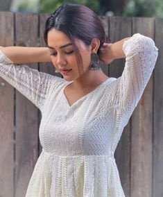 a woman in a white dress standing next to a wooden fence with her hands on her head