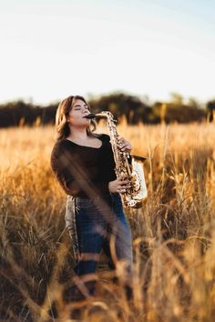 a woman standing in tall grass holding a saxophone and looking up at the sky with her eyes closed