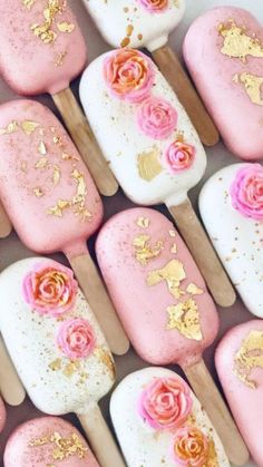 pink and gold decorated marshmallows are arranged on wooden skewers with flowers