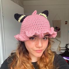 a young woman wearing a pink crocheted hat with black and yellow horns on it