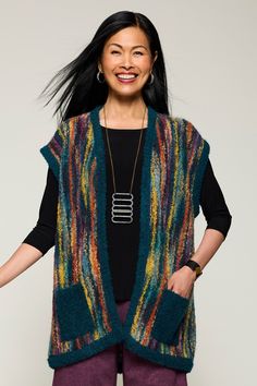 a woman with long black hair wearing a multicolored knitted vest and smiling at the camera