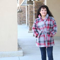 a woman standing on the sidewalk wearing a plaid coat