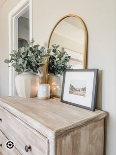 a white dresser with two potted plants on top and a framed photograph next to it