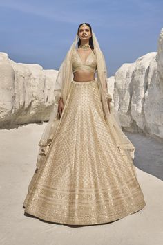 a woman in a gold lehenga standing on the beach with rocks behind her