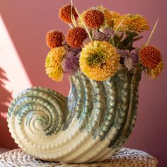 a vase filled with lots of flowers on top of a wicker table next to a pink wall