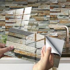 a person is holding up a piece of paper in front of a wall with stone tiles on it