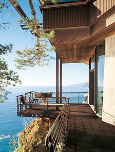 a balcony overlooking the ocean with wooden railings and chairs on it's sides