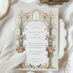 a wedding card with flowers and birds on it next to a feather quill pen