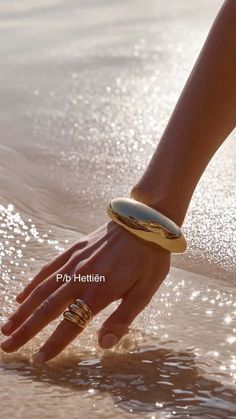 a woman's hand reaching into the water at the beach with her ring on it