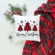 a christmas pillow sitting on top of a blanket next to a red and black plaid scarf