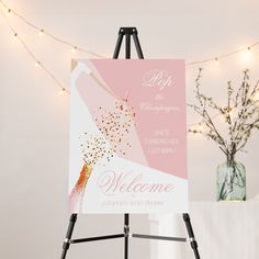 a welcome sign is on an easel next to a vase with flowers and lights