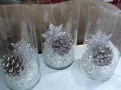 three clear glass vases with pine cones and snowflakes in them on a table