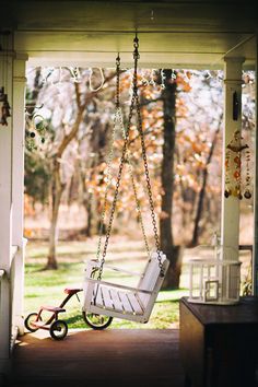 a swing chair hanging from a porch with a bicycle in the foreground and trees in the background