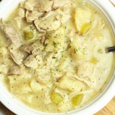 a white bowl filled with chicken and dumplings on top of a wooden cutting board