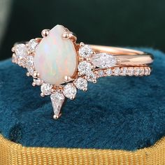 an opal and diamond ring sits on top of a blue velvet cushion