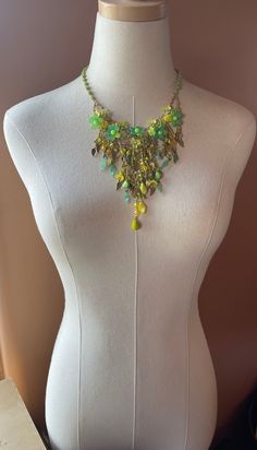 Colleen Toland Handmade Necklace circa late 90s.  This incredible necklace is made in stunning bright colors of green and yellow and gold.  The flowers are hand painted resin and are beaded together with glass seed beads.  The fringing is done with various uniquely shaped glass beads and metal and glass leaves that are rare to find today.  The necklace is wire wrapped with a square, matt green glass bead. The closure is a secure lobster claw with a signed metal tag so as it can be verified an original Colleen Toland work. The works shown in this shop are vintage Colleen Toland from past collections and they are the last of these pieces from Colleen's archive.  They are no longer in production and will not be remade.  They are not pre-owned and have never been worn.  They come with a certif Green Bohemian Necklace With Dangling Beads, Green Beaded Dangle Necklaces, Bohemian Green Beaded Chain Jewelry, Green Dangle Necklace With Beads, Green Necklaces With Dangling Beads, Green Costume Jewelry Beaded Necklace, Green Bohemian Beaded Necklaces, Green Costume Jewelry Necklace, Green Beaded Necklace With Dangling Beads For Party