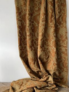 an orange and gold curtain hanging on a white wall next to a wooden floor in front of a window