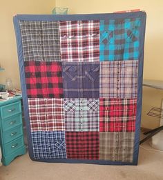 a bed room with a neatly made quilt on the wall and dressers in the background