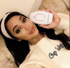 a woman laying on top of a couch holding a remote control in her hand and looking at the camera