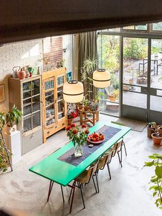 a dining room table and chairs with plants in the center, next to an open glass door